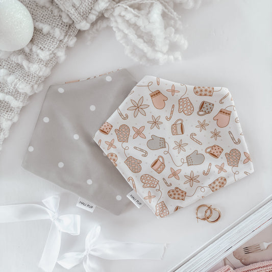 Two reversible dog bandanas laid out flat, one with a polkadot pattern and the other with a winter themed pattern