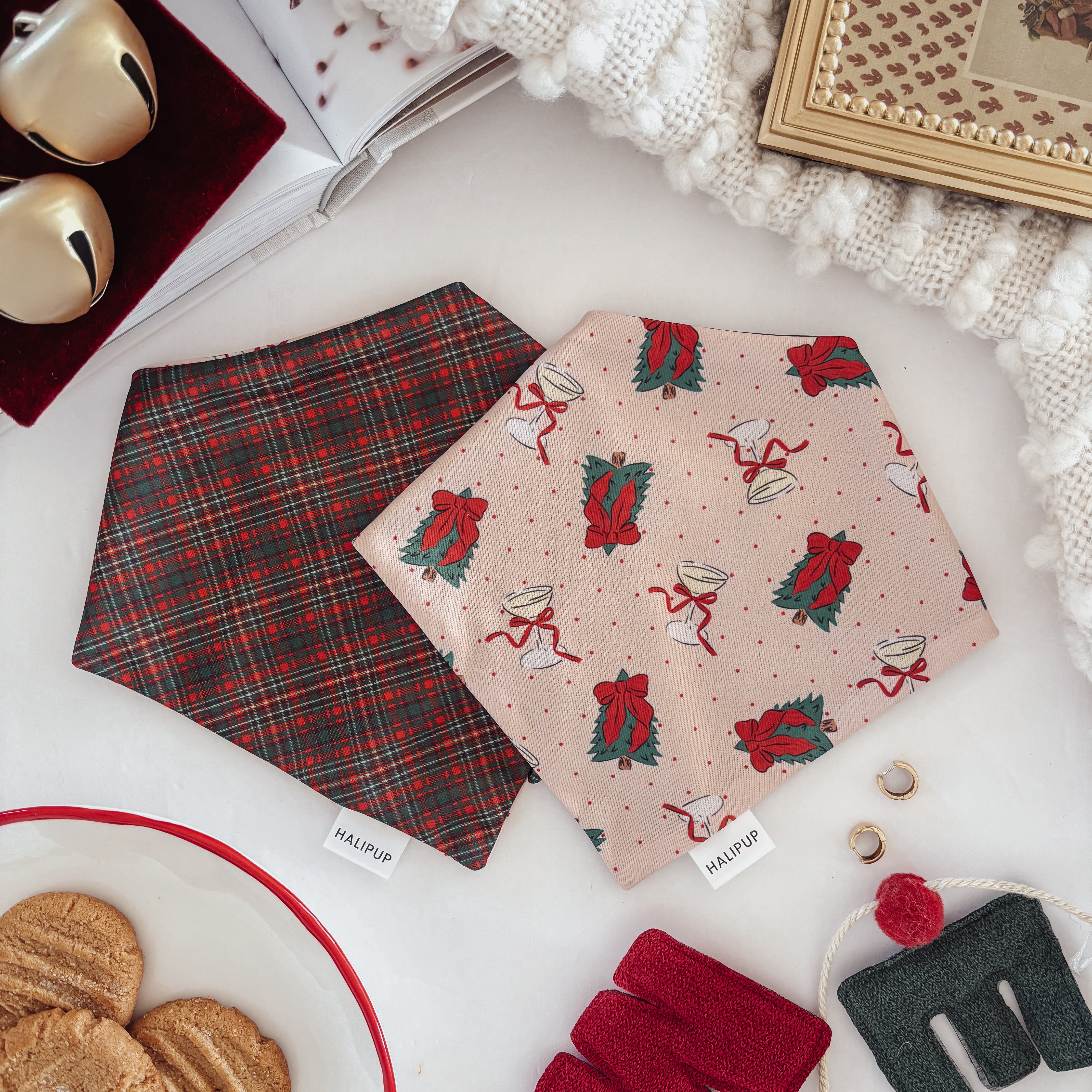 Two dog bandanas with Christmas patterns on a white surface with cookies and decorative items.